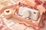 SipPixel gift concept with a white camera, peach gift box and ribbon beside a latte.